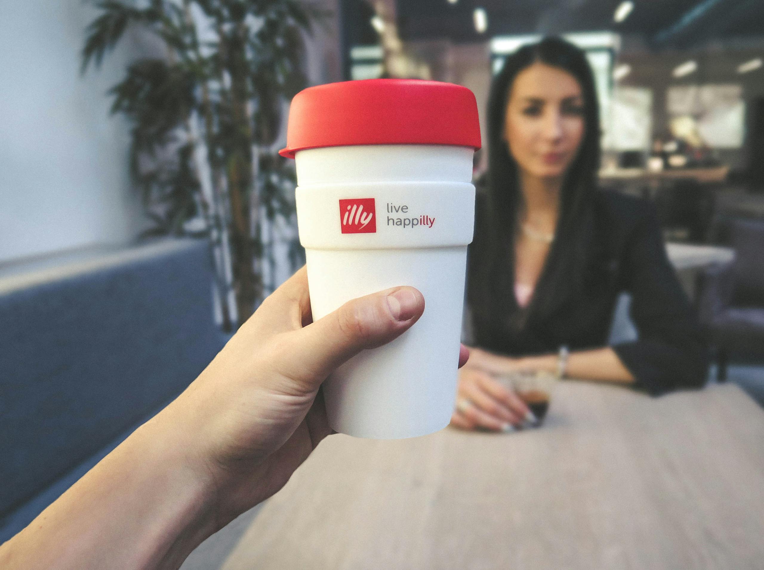 Focus on a reusable coffee cup with a woman in a business setting at a café.